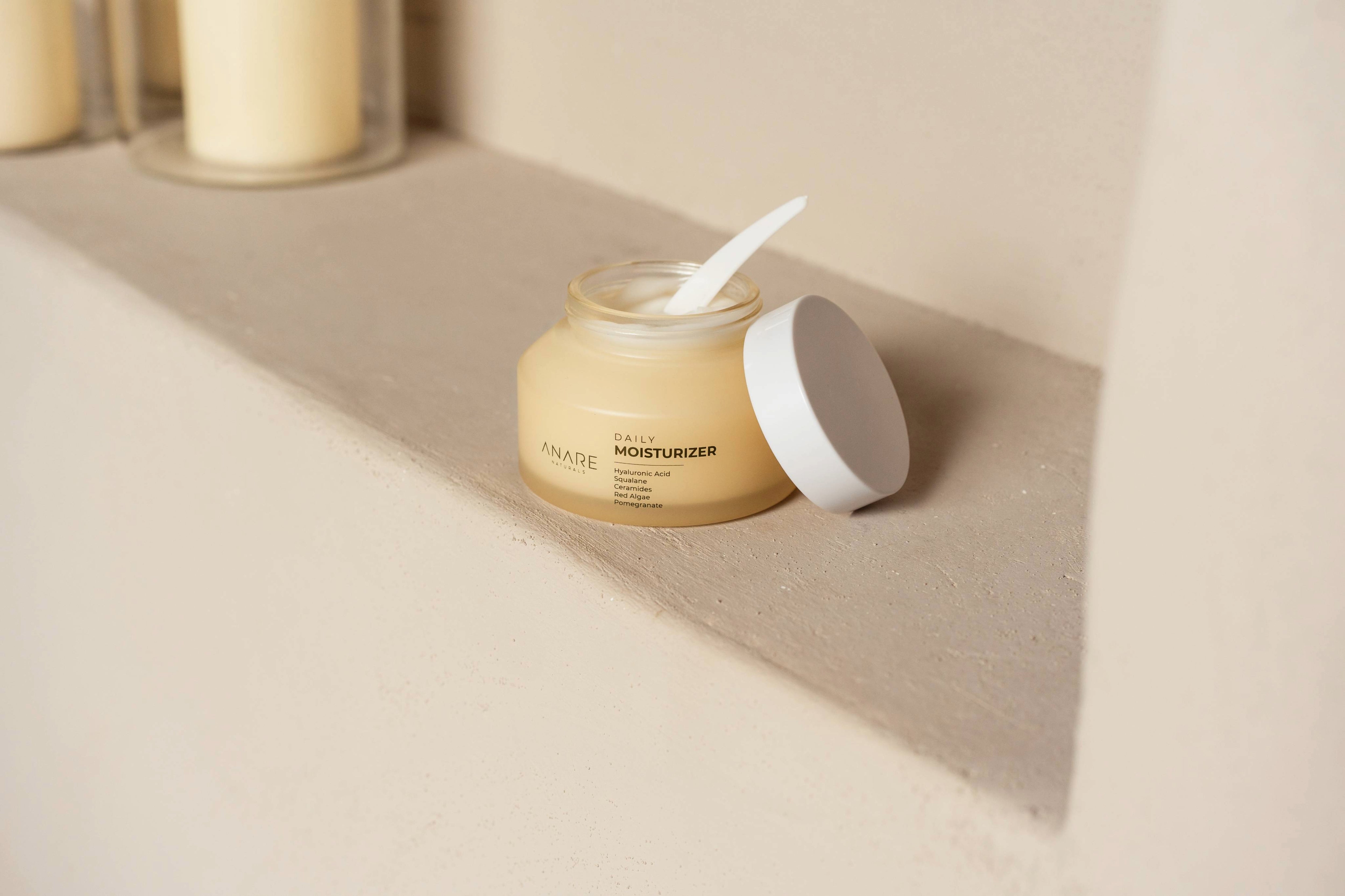 Anare Naturals Daily Moisturizer placed in the corner of an aesthetic light brown wall.