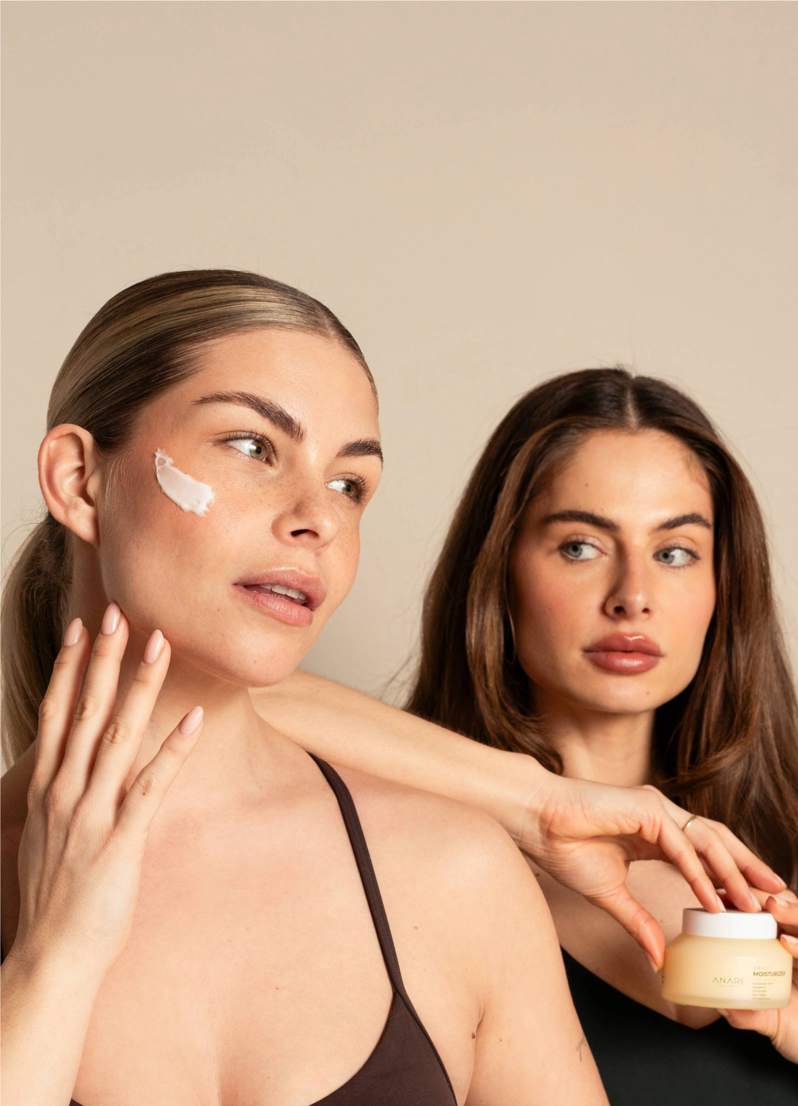 A blonde and brunette woman applying the Daily Moisturizer while holding the product, showcasing its lightweight texture and hydrating effect.