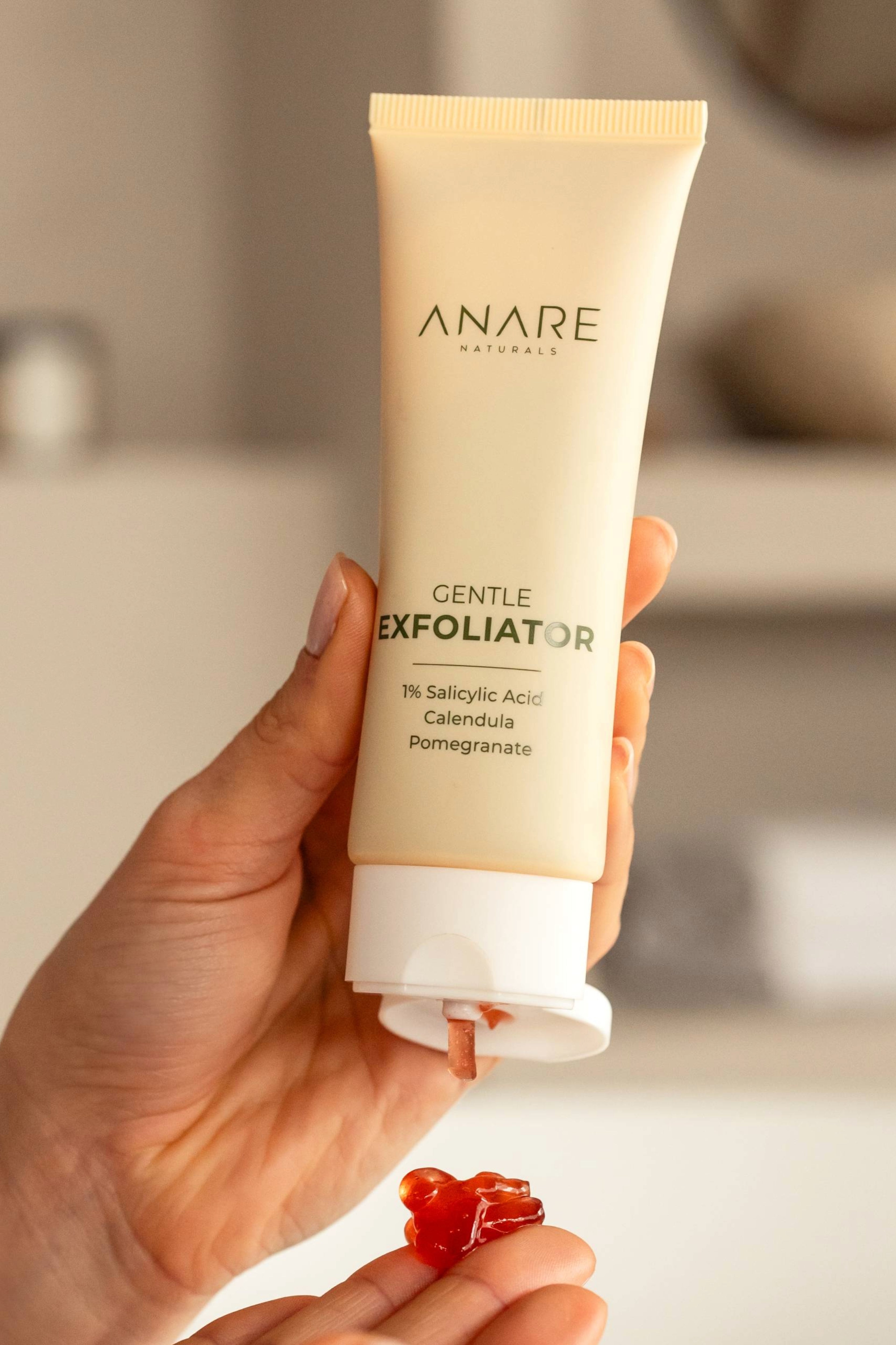 A tube of Gentle Exfoliator being squeezed, releasing a red gel infused with powerful skincare ingredients for smooth and radiant skin.