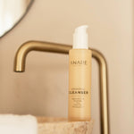 A sleek glass bottle of the Hydrating Cleanser resting on a bathroom sink, ready to refresh and cleanse your skin.